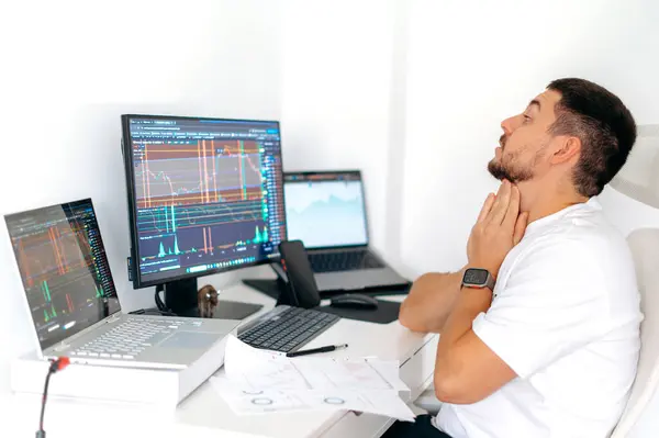 Surprised confused male crypto trader sitting at home at his work desk, shocked looks at computer screen, puzzled, had at big profits, currency growth, cant believe his eyes