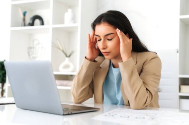 Yorgun düşmüş Arap ya da Hintli iş kadını, şirket CEO 'su, şirket avukatı, yönetici, ofiste bir masada oturuyor, şakaklarına masaj yapıyor, baş ağrısı, migren, stres, dinlenmeye ihtiyacı var.