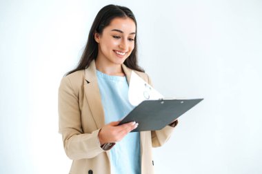 Kendinden emin, esmer, Hintli ya da Arap bir iş kadını, finansal danışman, tüccar, izole edilmiş beyaz arka planda duruyor, elinde belgeler ve grafiklerle klasörü tutuyor, ona bakıyor, arkadaşça gülümsüyor.