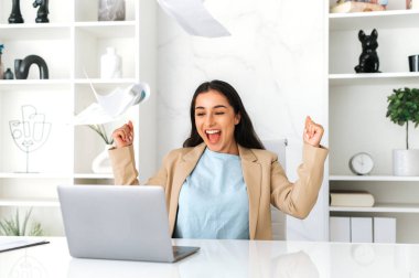 Şen şakrak, mutlu Hintli ya da Arap iş kadını şık kıyafetler içinde modern ofiste oturuyor, terfi etmekten keyif alıyor, büyük kar elde ediyor, dokümanları neşeyle fırlatıyor, eğleniyor, gülüyor, el kol hareketi yapıyor.