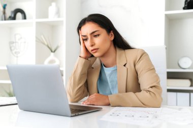Yorgun, genç, yetişkin Hintli ya da Arap iş kadını, şirket çalışanı, avukat, resmi giysiler içinde modern ofiste oturuyor, dizüstü bilgisayarda yorgun görünüyor, son teslim tarihi var, dinlenmeye ihtiyacı var.