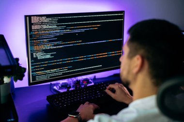 Başarılı programcı, yazılım geliştirici ve bilgisayar senaryosunun programlama kodları soyut teknolojisiyle bilgisayar ekranının önünde oturmuş, web kaynağı geliştirme üzerinde çalışıyor.