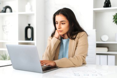 Şık bir takım elbiseli, modern bir ofiste çalışan, laptopa odaklanmış, bilgi okuyan, Hintli ya da Arap bir iş kadını.