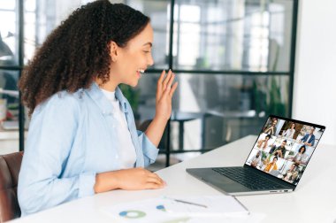 Brezilyalı iş kadını, ceo, takım lideri, ofiste dizüstü bilgisayarın önünde oturmuş, online video konferansında çok ırklı bir ekiple konuşuyor, beyin fırtınası yapıyor, gülümsüyor.