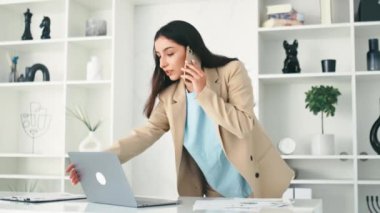 Meşgul başarılı Hintli ya da Arap iş kadını, şirket çalışanı, CEO, ofiste bir masanın yanında dur, akıllı telefonla konuş, ortak ya da müvekkil ile konuş, dizüstü bilgisayar kullan, gülümse.