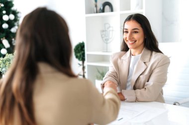 Anlaşma, işbirliği, tokalaşma. İki başarılı bayan meslektaşı bir masada oturuyor, modern ofis alanında fikirler ve planlama stratejisi tartışıyorlar, el sıkışıyorlar, projeyi onaylıyorlar.