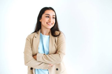 Zarif takım elbiseli güzel, kendine güvenen Hintli ya da Arap esmer kadın, izole edilmiş beyaz arka planda duruyor, kollarını kavuşturmuş, başka tarafa bakıyor, mutlu bir şekilde gülümsüyor.