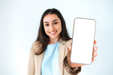 Kopya-uzay konsepti. Zarif takım elbiseli mutlu Hintli ya da Arap kadın, reklam için beyaz ekranı boş, beyaz arka planda duran akıllı telefonu gösteriyor, kameraya bakıyor, gülümsüyor.