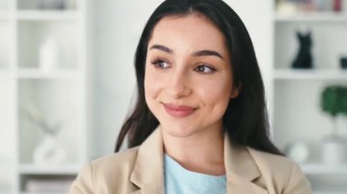 Güzel başarılı esmer Hintli ya da Arap kadın, CEO, emlak komisyoncusu, şirket yöneticisi, şık bir takım elbise giymiş, modern bir ofis yerinde duruyor, kameraya gülümsüyor.