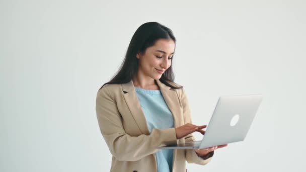 商业概念 漂亮而自信的印度或阿拉伯商业女性 穿着雅致西装的办公室职员 手持敞开式笔记本电脑 站在与世隔绝的白色背景上 看着相机 面带微笑地友善 — 图库视频影像