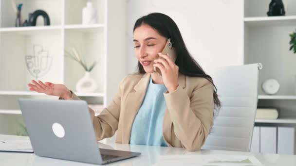 忙碌而成功的漂亮的印度或阿拉伯裔女商人 公司员工 Ceo坐在现代化的办公室里 用智能手机交谈 与伴侣或客户交谈 使用笔记本电脑 — 图库视频影像