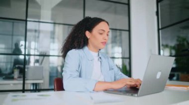 Hüsrana uğramış üzgün Brezilyalı ya da İspanyol kıvırcık saçlı iş kadını, şirket CEO 'su, finansal yönetici, modern bir yaratıcı ofiste oturuyor, üzgün bir şekilde dizüstü bilgisayara bakıyor, bilgi okuyor, kötü haber okuyor.