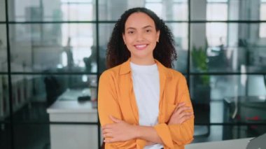 Kadın portresi. Gururlu, muhteşem, çok ırklı kıvırcık saçlı, sıradan kıyafetleri olan, modern ofiste, kollarını kavuşturup kameraya bakan, gülümseyen bir kadın.