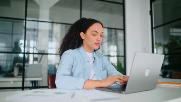 全神贯注地专注于工作的漂亮女人穿着淡蓝色衬衫 坐在现代办公室的办公桌前 在笔记本电脑上工作 专心致志地在笔记本上记笔记 — 图库视频影像