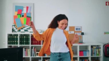 Eğleniyorum. Şık giyimli, kıvırcık saçlı, modern ofis çalışanı, neşeli bir şekilde dans eden mutlu, çok kültürlü genç kadın terfi aldı, iyi bir anlaşma yaptı, güldü, el kol hareketi yaptı.