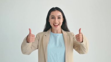 Mutlu Hintli ya da Arap esmer iş kadını, şık takım elbiseli, yönetici, kameraya zevkle bakıyor ve iki eliyle baş parmağını kaldırıyor, izole beyaz arka planda duruyor, gülümsüyor.