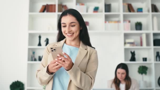女人用智能手机 穿着西装 站在办公室里 拿着手机 与朋友或客户在社交媒体上发短信 在网上下订单 微笑的阿拉伯裔或印度裔成功女性 — 图库视频影像