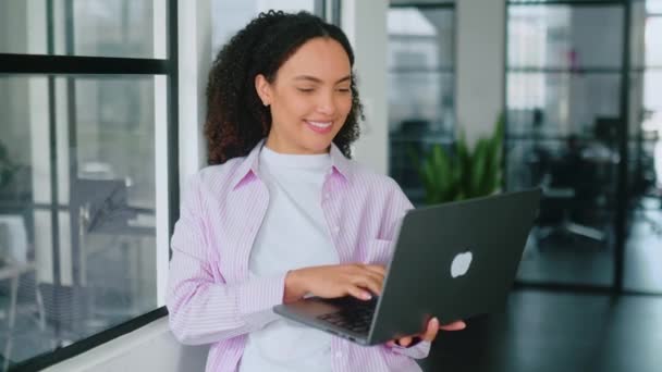 自信华丽的 成功的多种族 卷发的年轻女子 软件工程师 手握笔记本电脑 站在一个现代化的办公室里 看着相机 面带微笑地友善 免版税图库视频片段