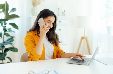 Cep telefonu sohbeti. Pozitif güzel Arap ya da Hintli genç kadın, ürün yöneticisi, web tasarımcısı, bir dizüstü bilgisayarda çalışıyor, müşterisiyle akıllı telefon konuşması yapıyor.