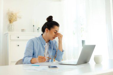 Arap ya da Hint kökenli yorgun ve stresli bir iş kadını mavi gömlekli, şirket CEO 'su, bir dizüstü bilgisayarla çalışırken bir iş yerinde oturur, kendini çok yorgun hisseder, gözlerini kapatır ve Bridgenose' a masaj yapar.