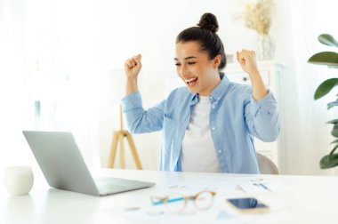 Neşe, keyif. Neşeli mutlu Hintli ya da Arap başarılı iş kadını, bir iş yerinde oturuyor, bir dizüstü bilgisayara bakıyor, başarıyla seviniyor, iyi iş sonuçları, gülümsüyor, elleriyle hareket ediyor.