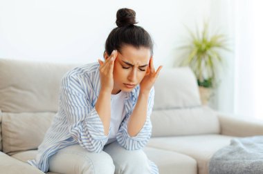 Stres, baş ağrısı, hastalık. Oturma odasında gözleri kapalı, baş ağrısı, baş dönmesi, baş dönmesi, migren, bir şakaksızda kramp geçiren, tedavi edilmesi ve dinlenmesi gereken melez bir kadın.