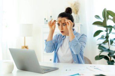 Arap ya da Hint uyruklu heyecanlı bir kadın gözlüklü, ofis çalışanı, sürpriz kaldırma gözlükleriyle laptop ekranına bakıyor, internette beklenmedik bilgiler görüyor.