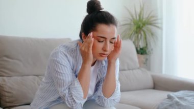 Stres, baş ağrısı, hastalık. Oturma odasında gözleri kapalı, baş ağrısı, baş dönmesi, baş dönmesi, migren, bir şakaksızda kramp geçiren, tedavi edilmesi ve dinlenmesi gereken melez bir kadın.
