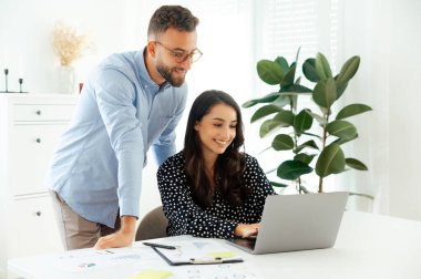 Erkek, masa başında dizüstü bilgisayar üzerinde çalışırken kadın meslektaşına yardım ediyor, modern bir ofiste profesyonel takım çalışması yapıyor, pozitif iş arkadaşları bir proje üzerinde birlikte çalışıyor, fikirler geliştiriyor ve iş planı geliştiriyor.