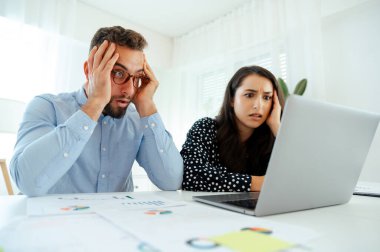 Bir dizüstü bilgisayardaki veri ve çizelgeleri analiz eden, ofiste otururken bir sorunu çözmek için birlikte çalışan, kafa karışıklığı ve hayal kırıklığı yaşayan, kafası karışık iş arkadaşları.