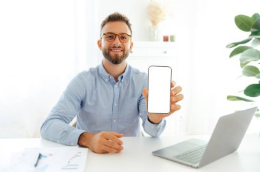 Ofisteki bir masada oturan ve boş bir ekranlı akıllı telefonu gösteren başarılı bir iş adamı. Uygulamalar veya reklamlar için model görüntüleme konsepti, sunum