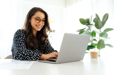 Neşeli esmer beyaz ya da Arap iş kadını, beyaz bir masada oturuyor, ofiste belgelerle çevrili, iyi haberler okuyor, müşterilerle ya da iş arkadaşlarıyla mektuplaşıyor, gülümsüyor.