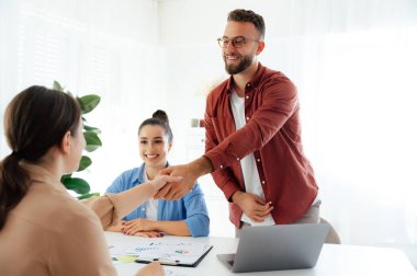 Takım çalışması. Başarılı bir anlaşma. Meslektaşlar birbirlerine gülümserken el sıkışıyorlar. İş ortaklarından oluşan bir grup bir proje üzerinde ofiste birlikte çalışıyor, anlaşma yapıyor, işbirliği planlıyor.