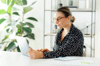 Kendine güvenen başarılı bir iş adamı, bir proje üzerinde çalışırken bilgisayarına odaklanmış, ofiste otururken bilgileri tarıyor ve analiz ediyor, gülümsüyor.
