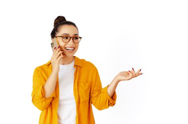 Sarı gömlekli ve gözlüklü mutlu beyaz kadın akıllı telefonuyla konuşuyor, elini sallıyor ve gülümsüyor, izole edilmiş beyaz bir arkaplanda duruyor. Mobil iletişim kavramı