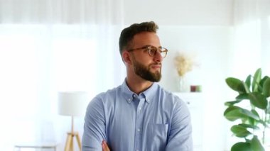 Mavi gömlekli, kendine güvenen sakallı bir iş adamının videosu. Parlak, modern bir ofiste dikilirken sıcak bir şekilde gülümsüyor. Başarı kavramı, pozitiflik ve profesyonel güven