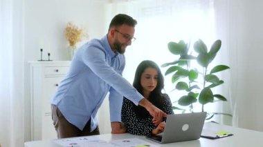 İki başarılı meslektaş. Gözlüklü profesyonel bir genç adam gülümseyen esmer bir kadının üzerine eğiliyor. Modern bir ofiste iş görüşmesi sırasında dizüstü bilgisayarı işaret ediyor. Takım çalışması konsepti.