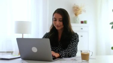 Uzun siyah saçlı, hoş bir iş kadını. Gömlek giymiş, şirket müdürü. Masasında dosyalar ve kameraya gülümserken dizüstü bilgisayarda yazı yazıyor.