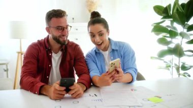 Şok olmuş bir adam ve kadın ofislerinde bir masada oturmuş, akıllı telefonlarını kullanıyor, ekranlara bakıyor, beklenmedik haberler okuyor, şaşırtıcı bilgiler alıyor, gösteriler mutlu duygular yaşıyor, oyunlar oynuyor.