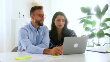 Başarılı bir adam ve kadın bir masada oturuyor, belgeleri ve çizelgeleri birlikte inceliyor, ekrandaki detayları inceliyor, fikirleri paylaşıyor ve gülümsüyor, takım çalışması kavramını anlatıyor.
