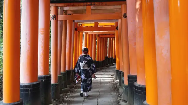 Kimono giymiş bir kadın Fushimi Inari Tapınağı 'nda Torii kapılarının altından yürüyor..