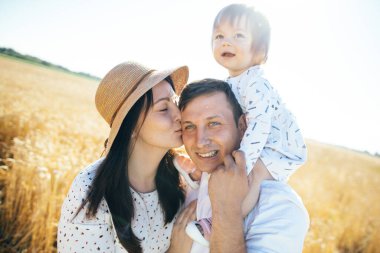 Mutlu bir yaz yürüyüşü yapan aile, anne, baba ve çocuk buğday tarlasında yürüyor ve gün batımında güzel doğanın tadını çıkarıyor. Yüksek kalite fotoğraf