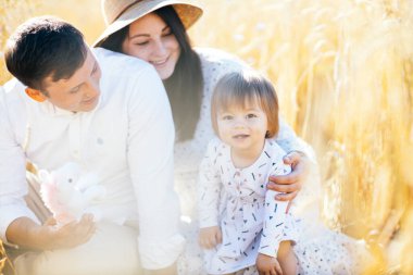 Mutlu bir çocukluk, aile buğday tarlasında yürüyor. Anne, baba ve küçük kız birlikte dışarıda vakit geçiriyorlar. Ebeveynler ve çocuklar yaz otlaklarında oynuyorlar. Yüksek kalite fotoğraf