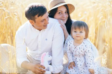 Mutlu bir çocukluk, aile buğday tarlasında yürüyor. Anne, baba ve küçük kız birlikte dışarıda vakit geçiriyorlar. Ebeveynler ve çocuklar yaz otlaklarında oynuyorlar. Yüksek kalite fotoğraf