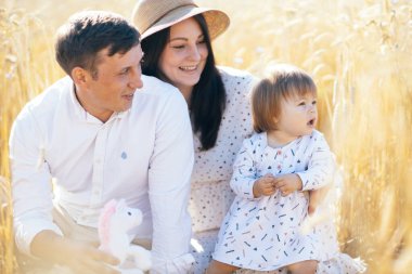 Mutlu bir çocukluk, aile buğday tarlasında yürüyor. Anne, baba ve küçük kız birlikte dışarıda vakit geçiriyorlar. Ebeveynler ve çocuklar yaz otlaklarında oynuyorlar. Yüksek kalite fotoğraf