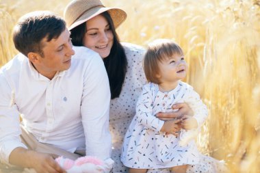 Mutlu bir çocukluk, aile buğday tarlasında yürüyor. Anne, baba ve küçük kız birlikte dışarıda vakit geçiriyorlar. Ebeveynler ve çocuklar yaz otlaklarında oynuyorlar. Yüksek kalite fotoğraf