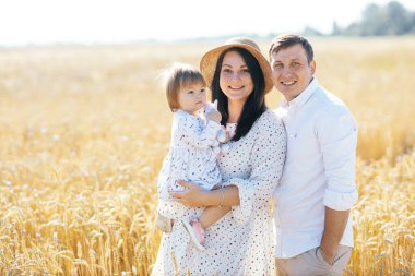 Mutlu bir yaz yürüyüşü yapan aile, anne, baba ve çocuk buğday tarlasında yürüyor ve gün batımında güzel doğanın tadını çıkarıyor. Yüksek kalite fotoğraf