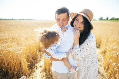 Mutlu bir yaz yürüyüşü yapan aile, anne, baba ve çocuk buğday tarlasında yürüyor ve gün batımında güzel doğanın tadını çıkarıyor. Yüksek kalite fotoğraf