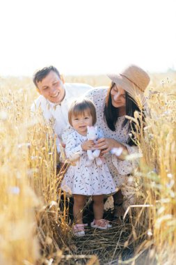 Mutlu bir yaz yürüyüşü yapan aile, anne, baba ve çocuk buğday tarlasında yürüyor ve gün batımında güzel doğanın tadını çıkarıyor. Yüksek kalite fotoğraf