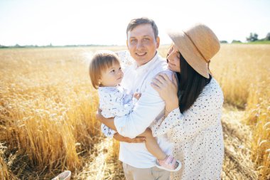 Mutlu bir çocukluk, aile buğday tarlasında yürüyor. Anne, baba ve küçük kız birlikte dışarıda vakit geçiriyorlar. Ebeveynler ve çocuklar yaz otlaklarında oynuyorlar. Yüksek kalite fotoğraf